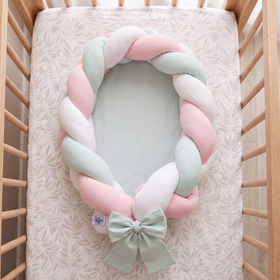 Réducteur de lit tressé rose, menthe et blanc sur drap à motif feuillage, lit à barreaux