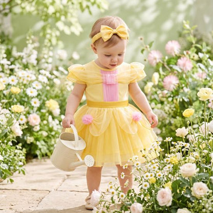 Bébé en tenue de fête jaune avec arrosoir dans un jardin fleuri