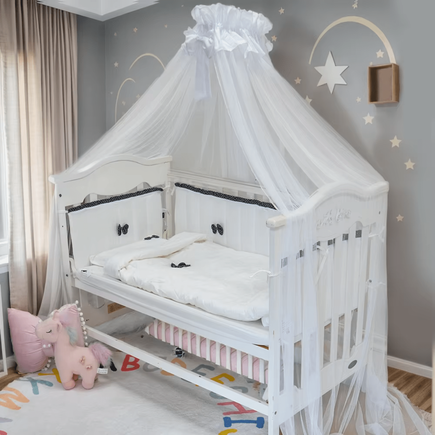 Tour de lit bébé blanc avec nœuds noirs installé dans un berceau en bois clair.