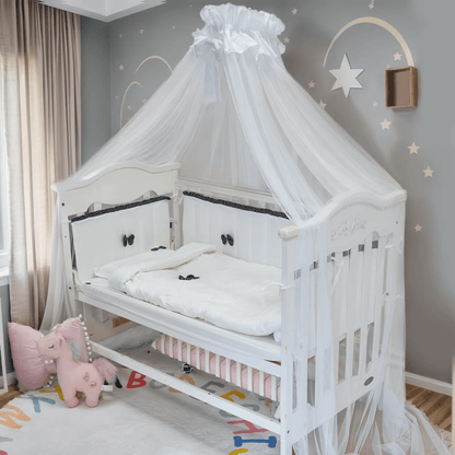 Tour de lit bébé blanc avec nœuds noirs installé dans un berceau en bois clair.