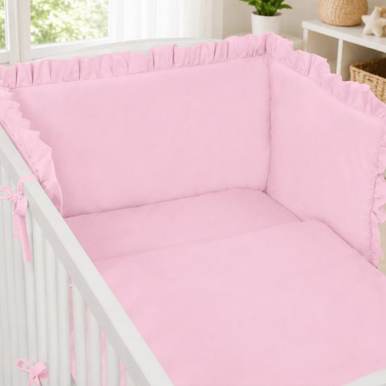 Tour de lit rose pour fille installé dans un lit bébé à barreaux blancs