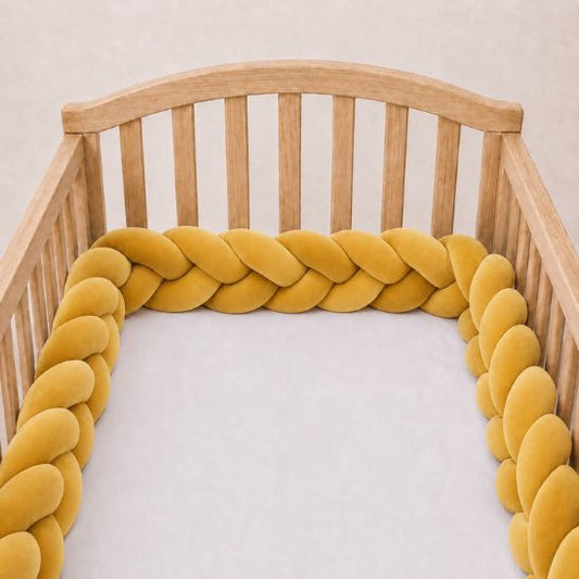 Tresse de lit bébé moutarde installée le long d'un lit à barreaux
