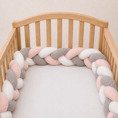 Tresse de lit bébé multicolore rose, gris et blanc installée le long d'un berceau en bois