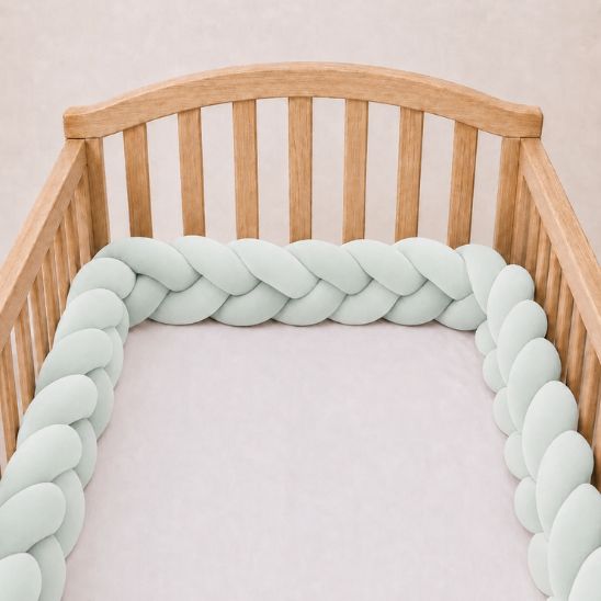 Tresse de lit bébé vert d'eau installée le long d'un lit à barreaux