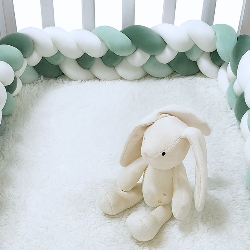 Doudou lapin posé dans un lit entouré d’une tresse vert sauge