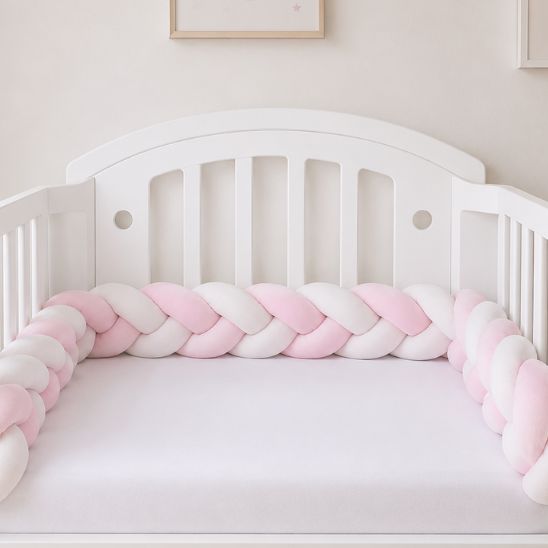 Tresse de lit rose et blanc installée tout le long d'un lit à barreaux bébé