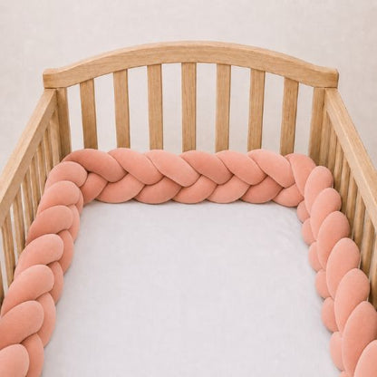 Tresse de lit rose saumon installée le long d'un lit bébé à barreaux