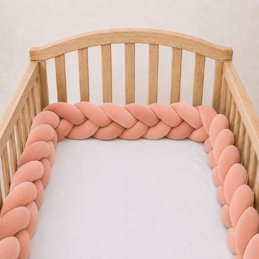 Tresse de lit rose saumon installée le long d'un lit bébé à barreaux