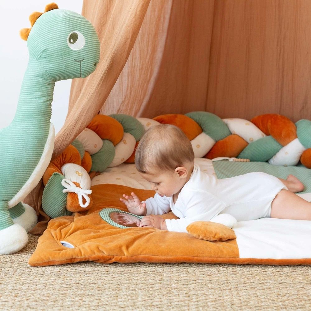 Bébé allongé dans son lit avec une Tresse de lit bébé 3 brins vert sauge et camel en décoration dans une chambre d’enfant.