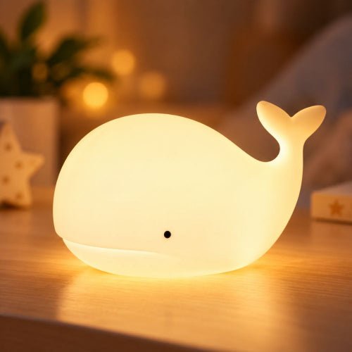 Veilleuse baleine blanche allumée en lumière chaude sur une table de chevet en bois