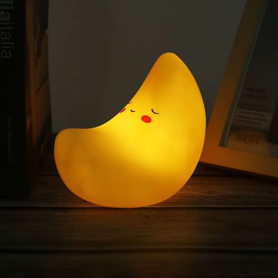 Veilleuse bébé lune en silicone jaune avec lumière chaude posée sur une étagère en bois