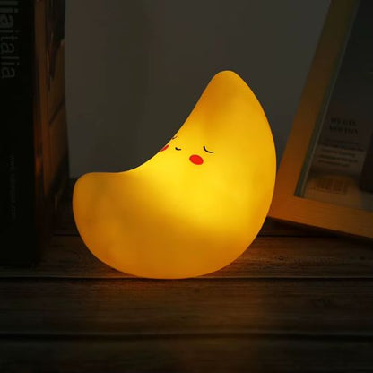 Veilleuse bébé lune en silicone jaune avec lumière chaude posée sur une étagère en bois
