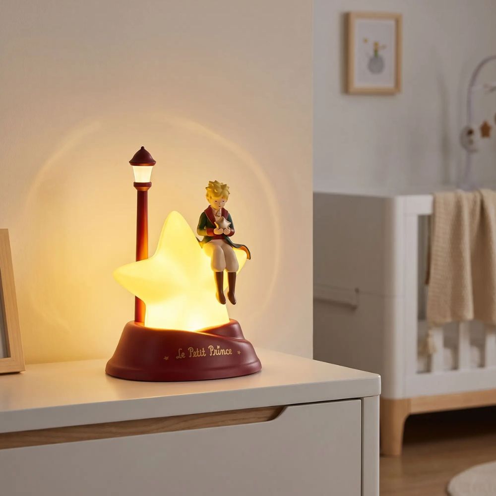 Veilleuse Le Petit Prince allumée sur une commode dans une chambre de bébé