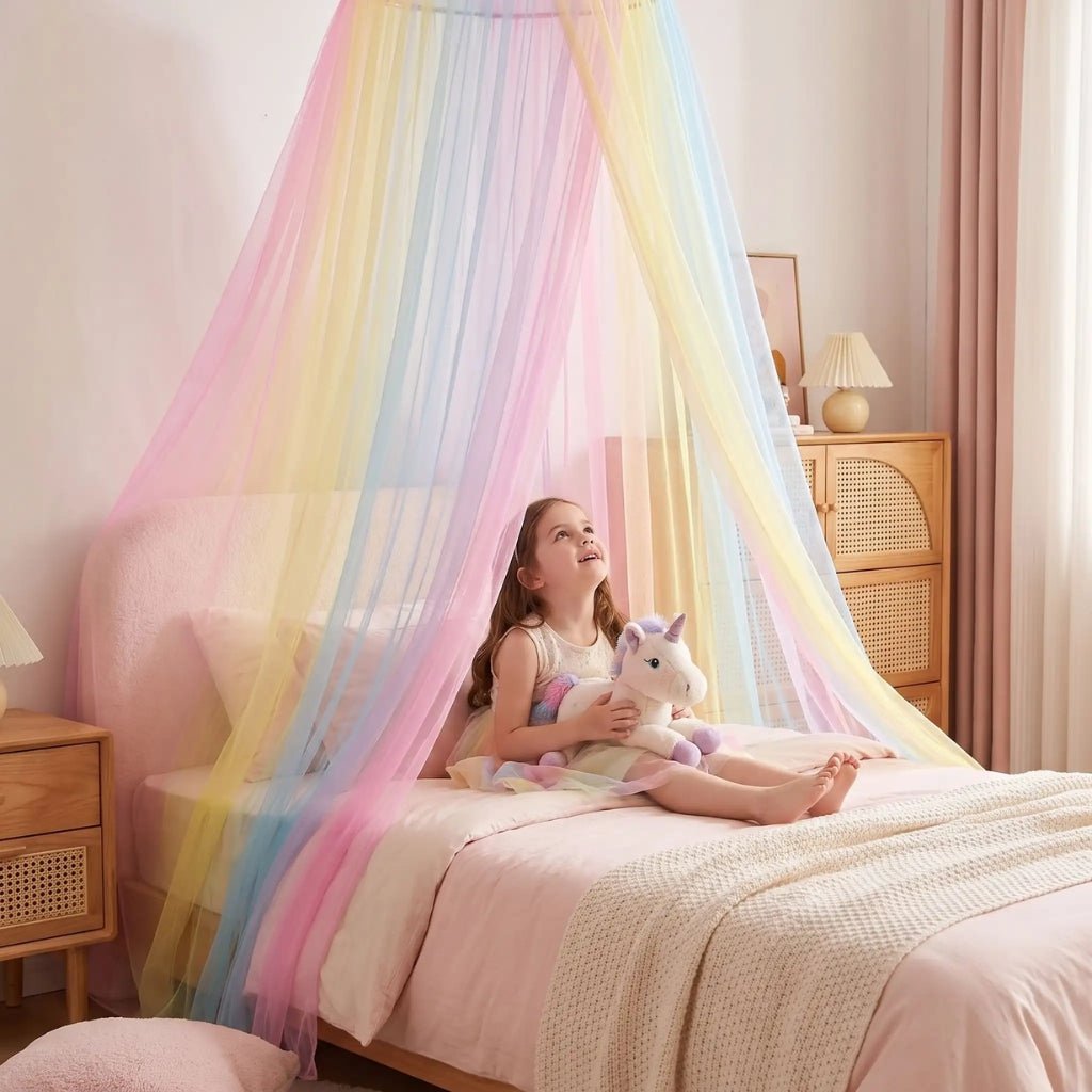 Petite fille avec sa licorne en peluche sur son lit sous un voile arc-en-ciel en tulle